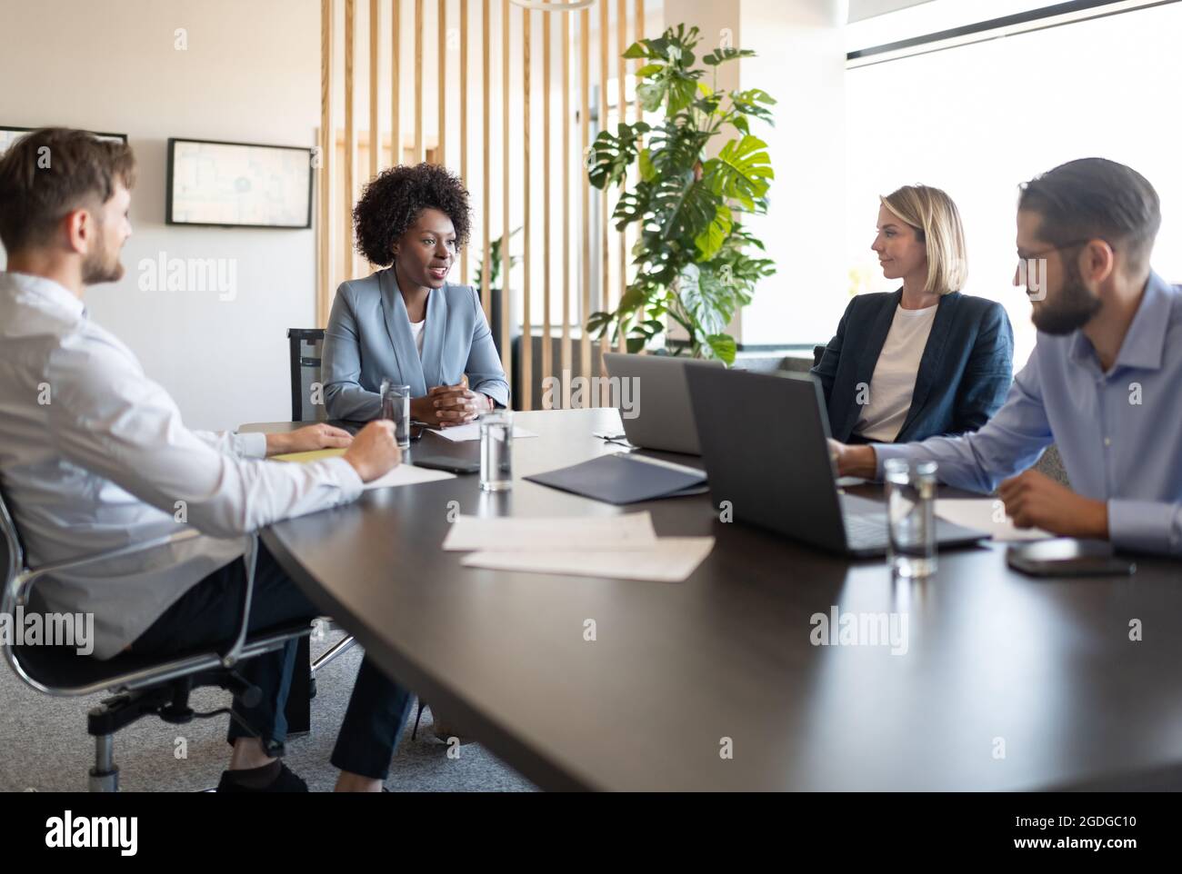 Büroangestellte sitzen am Tisch und hören während der Konferenz dem schwarzen Leiter zu Stockfoto