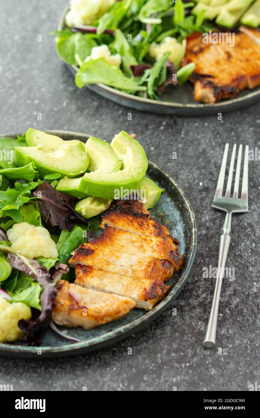 Abendessen auf dem Tisch, ein Teller gebratenes Schweinesteak und ein gemischter Salat mit Blumenkohl und Avocado Stockfoto