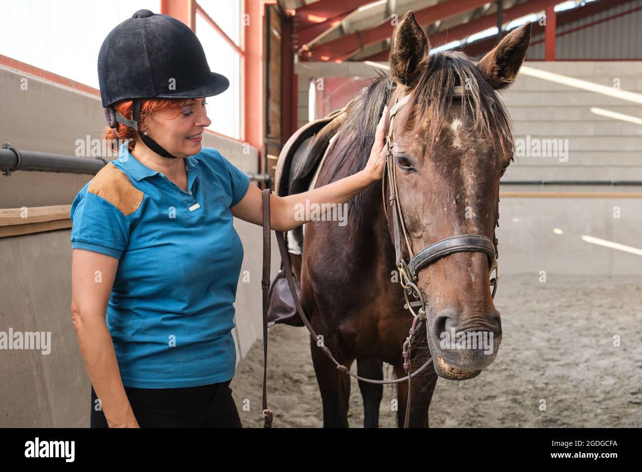 Frau lächelt und streichelt liebevoll ein Pferd in einem Stall. Stockfoto