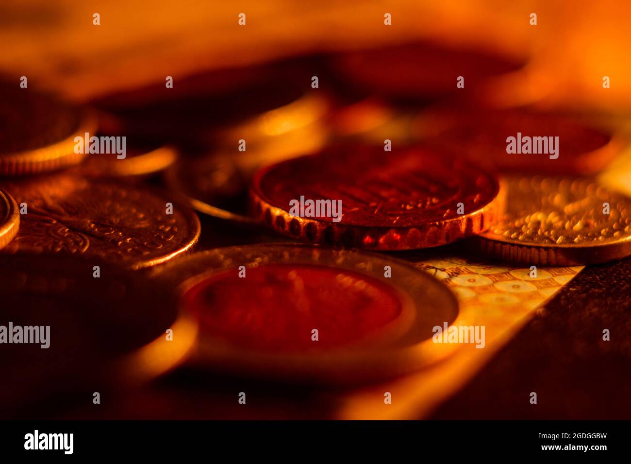 Nahaufnahme von Münzen und Banknoten, die auf einer mit hellem rotem Licht beleuchteten Oberfläche verstreut sind Stockfoto