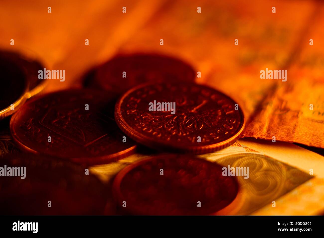 Nahaufnahme von Münzen und Banknoten, die auf einer mit hellem rotem Licht beleuchteten Oberfläche verstreut sind Stockfoto