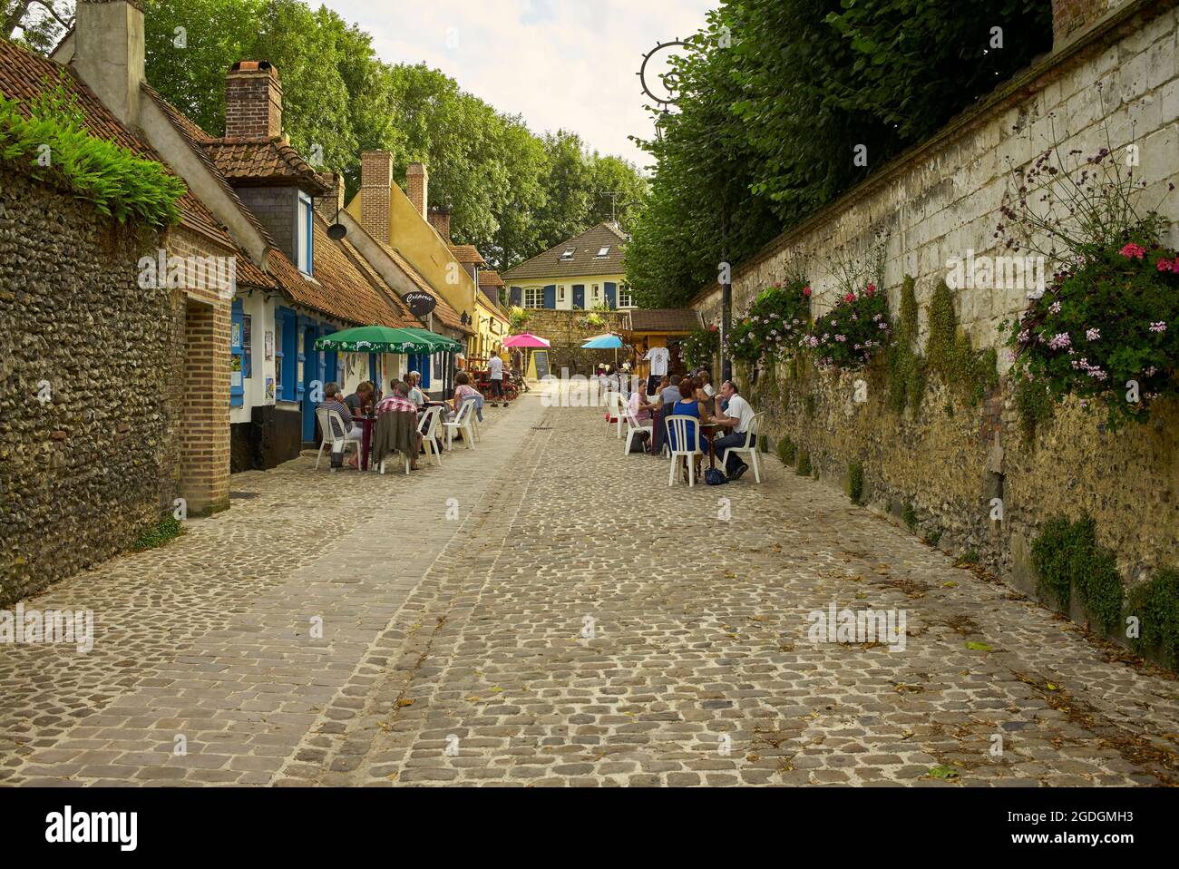 Touristen und Einheimische sitzen vor einer Bar in der Nähe der Stadtmauern der beliebten Stadt Montreuil sur Mer, Nord Pais de Calais, Frankreich. Stockfoto