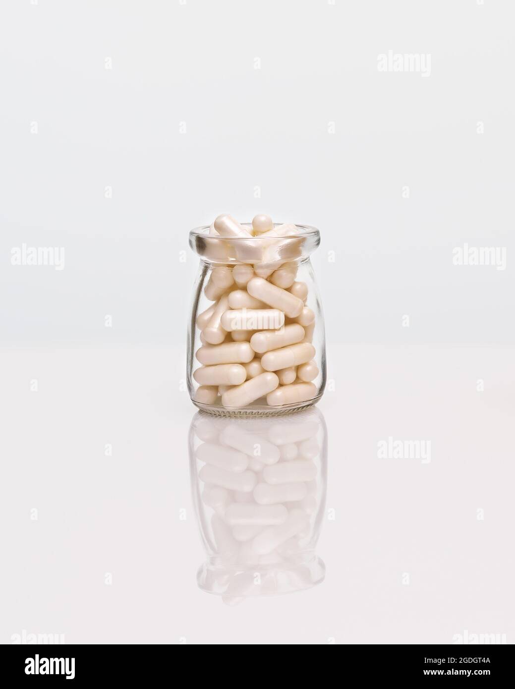 Weiße Kapseln in einer Glasflasche auf einem weißen Tisch mit Spiegelung. Vitaminkapseltabletten. Pharmaindustrie. Natürliche Kräuter, Stärkung der Immunität, Stockfoto