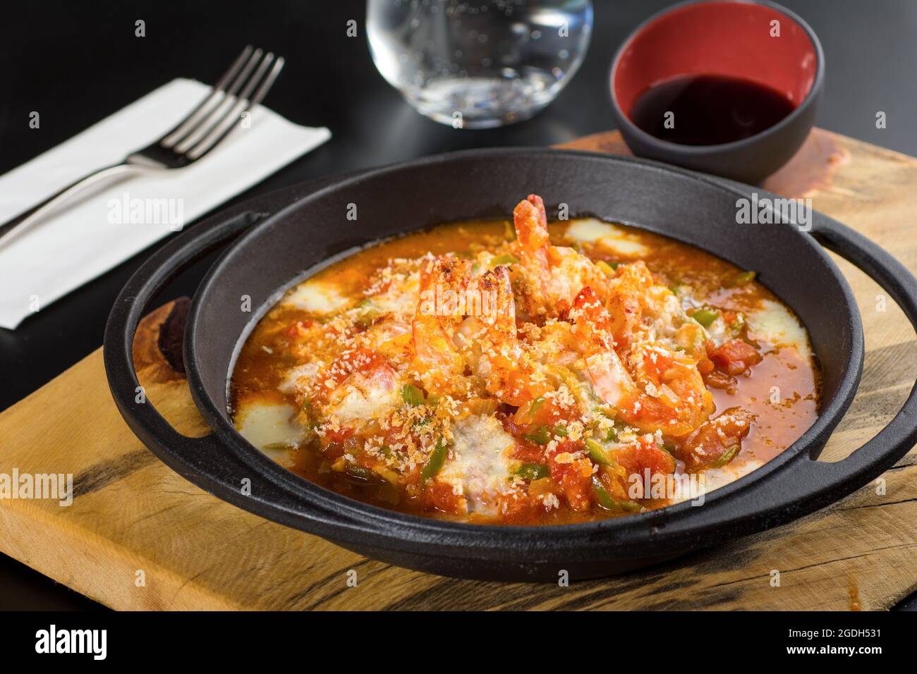 Garnelenauflauf mit Tomaten und Paprika in einer schwarzen Steinpfanne. Stockfoto