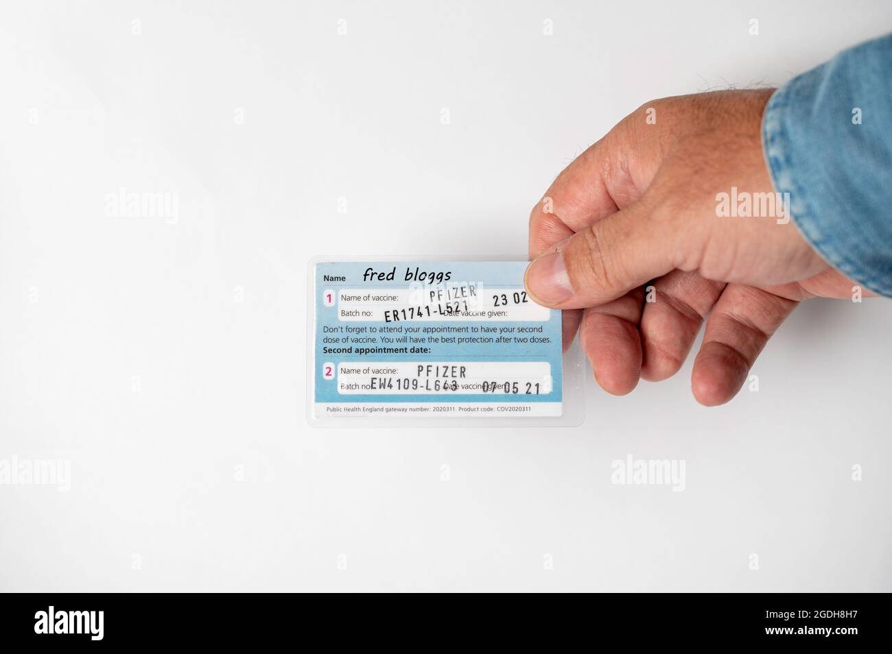 Englische handgehaltene Impfkarte mit einem fiktiven Namen, der die Daten beider Impfstoffe anzeigt Stockfoto