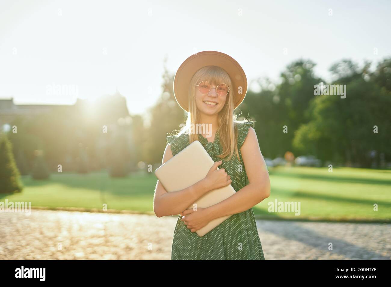 Liebenswert junge blonde Universität oder College-Student Mädchen mit Laptop trägt grünes Kleid und Hut auf dem Campus der Universität. Glückliche weibliche Schule oder Schülerin, pädagogisches Konzept. Hochwertige Bilder Stockfoto