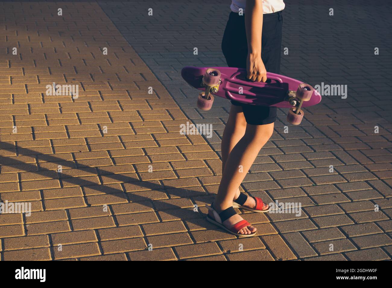 Ein Mädchen mit einem Skateboard in der Hand in der Abendsonne auf den Bürgersteig Fliesen Stockfoto
