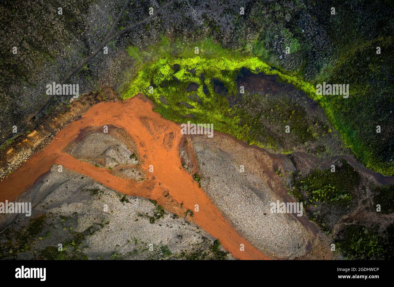 Luftaufnahme des Stromes von orangefarbenem Wasser, der durch raues moosiges Gelände in Island fließt Stockfoto