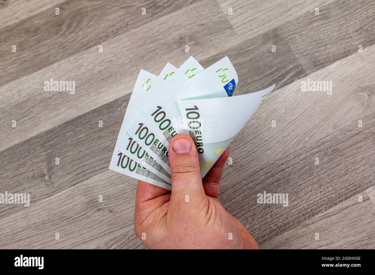 Hand des Mannes, der 100 Euro-Banknoten auf einem Holztisch zählt Stockfoto