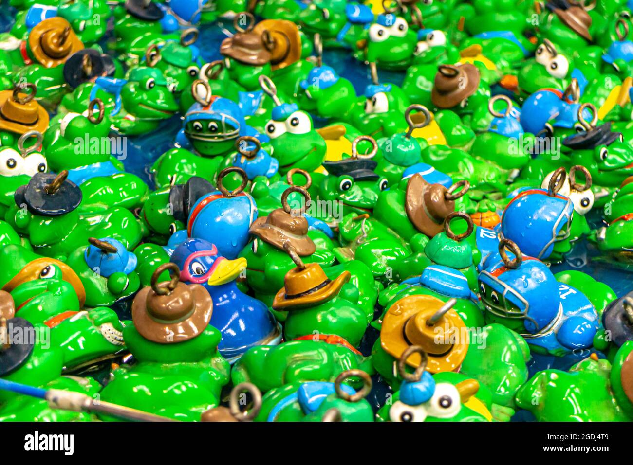 Kinderspiel Entenfischen auf einem Jahrmarkt. Viele grüne und blaue Plastikfrösche und Plastikenten in einem Wasserbecken mit einem Ring zum Angeln auf der Luftröhre Stockfoto