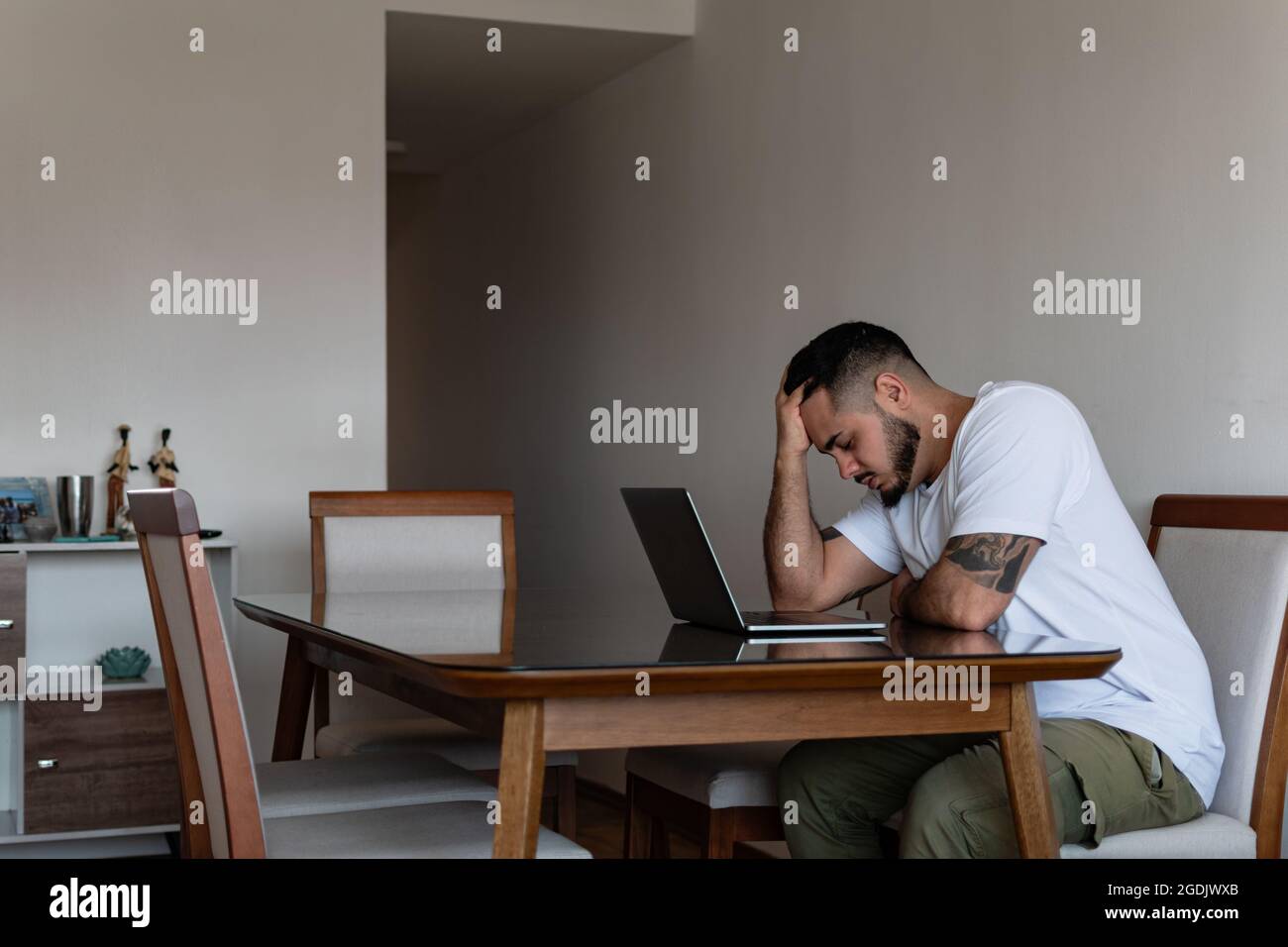 Der junge tätowierte lateinische Mann vor dem Laptop stresste heraus und hielt seinen Kopf fest Stockfoto