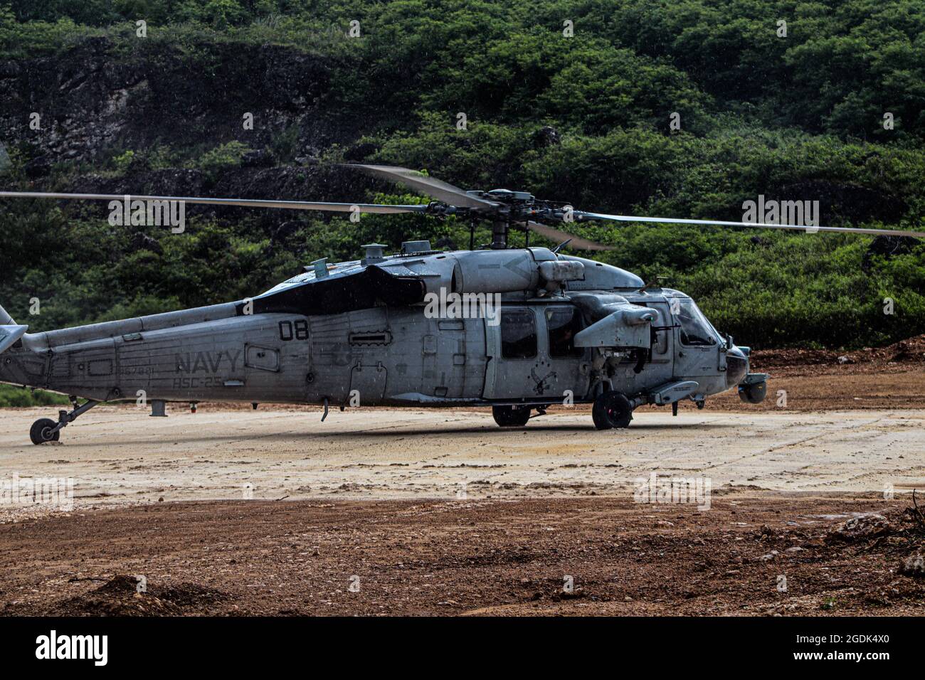 210803-N-MO469-1010 SANTA RITA, Guam (Aug 3, 2021) die dem HSC-25 zugewiesene Luftbesatzung landet eine MH-60S auf einem Prototyp-Landeplatz, der von Seabees gebaut wurde und dem Naval Mobile Construction Bataillon (NMCB) 11 det. Guam. Die Landeplatz wurde unter der Unterstützung von III MEF mit einem Biozement-Applikationssystem konstruiert, das von bioMASON mit Unterstützung der Defense Advanced Research Projects Agency entwickelt wurde. Das Biozement-Anwendungssystem wurde für den Einsatz in Vorwärtsoperationspositionen auf nativen, nicht entwickelten Oberflächen entwickelt, um den Boden zu stärken, die Erosionskontrolle zu fördern und die Staubentwicklung zu erhöhen Stockfoto