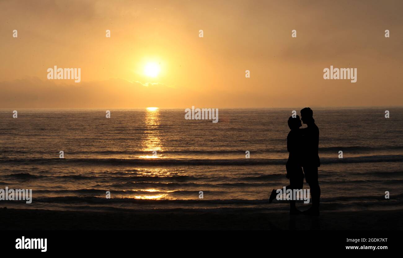 Liebhaber am Strand bei Sonnenuntergang. Glückliches Paar küssen und umarmen vor Sonne und Meereswellen. Romantisches Lover-Konzept. Stockfoto