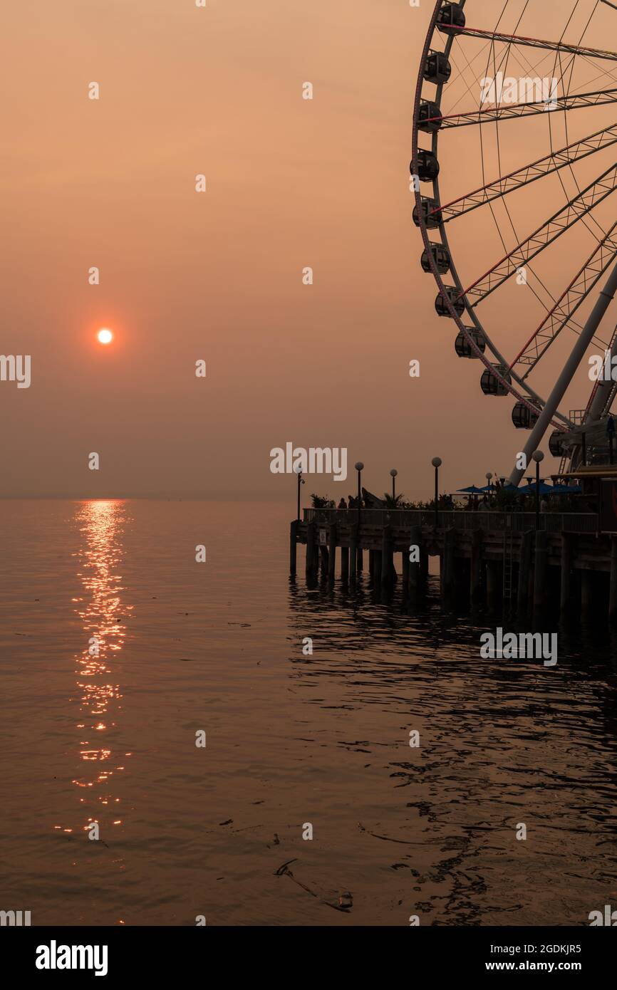 Seattle, USA. 13 August 2021. Menschen, die BergarbeiterInnen besuchen Landing spät am Tag als die anhaltende Hitzewelle die Stadt in die Mitte der 90er Jahre treibt, ist der Himmel von einem dicken orangen Dunst aus Feuerrauch erstickt. Seattleiten mussten lernen, in der zweiten Hälfte der Sommer mit dem jetzt regelmäßig rauchigen Himmel zu leben. Klimabrände wüten jährlich im gesamten PNW und senken für viele die Luftqualität und die Lebensqualität erheblich. James Anderson/ Alamy Live News Stockfoto