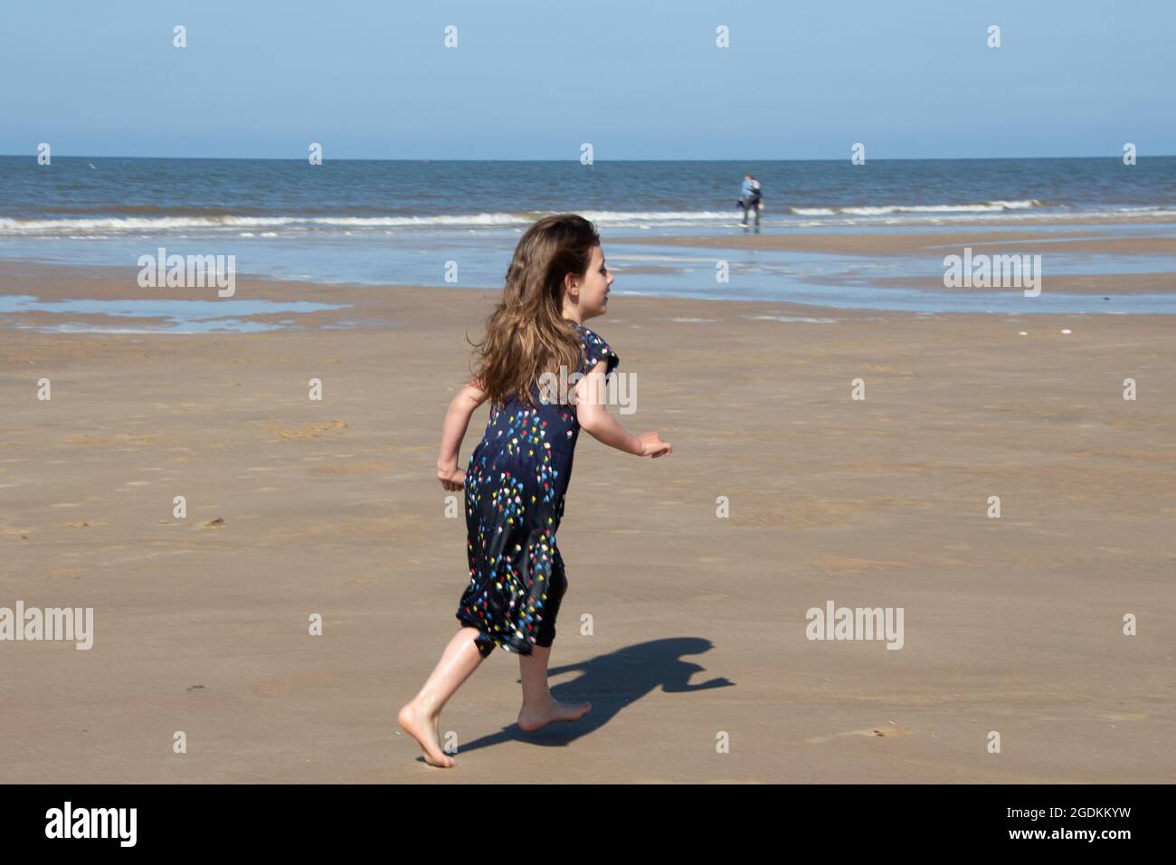 Junges Mädchen, das am Strand läuft, nördliche Küste, Cromer, England, blaues Kleid Stockfoto