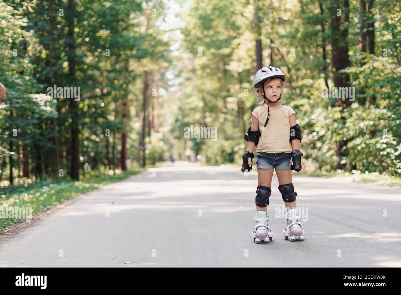 Kleines hübsches Mädchen auf Rollschuhe im Helm in einem Park. Fröhliche  Vorschulmädchen tragen Inline-Rollschuhe und Schutzausrüstung  Stockfotografie - Alamy