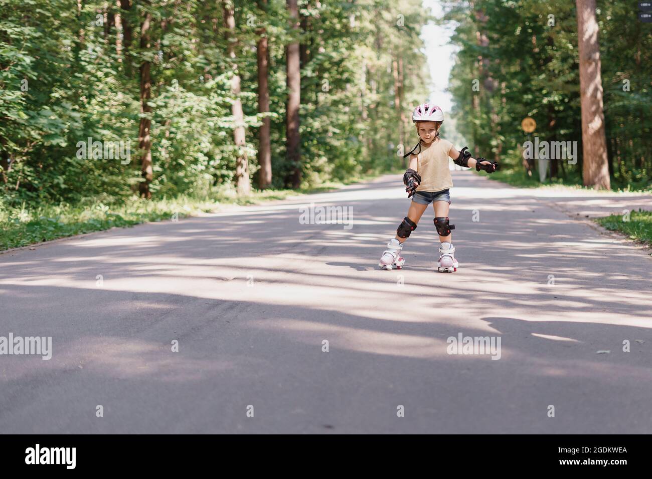 Kleines Mädchen ist Rollerblading im Park. Baby in schützender Sportkleidung Stockfoto