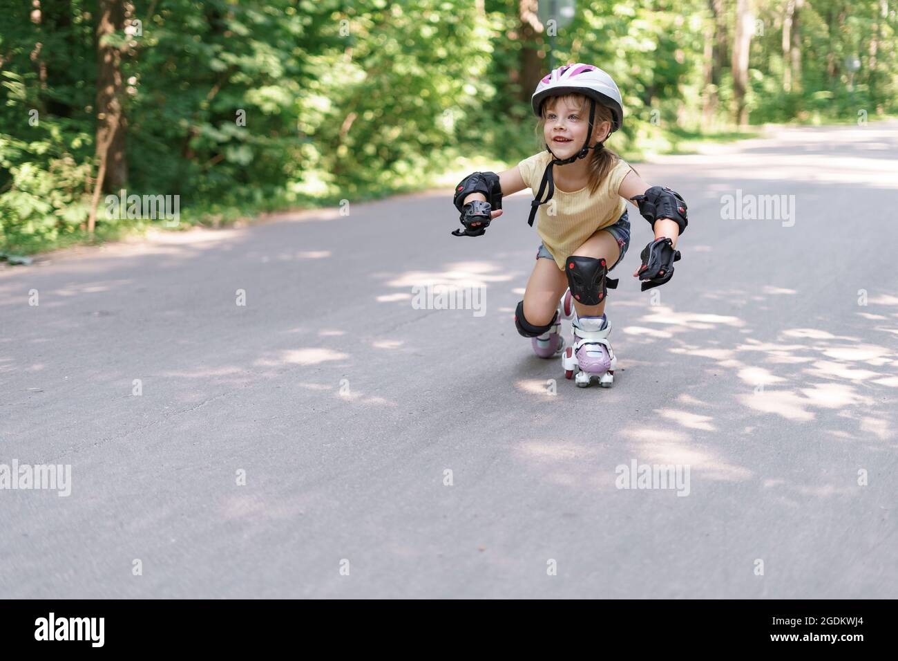 Baby in schützender Sportkleidung. Kleines Mädchen, das Rollschuh lernt Stockfoto