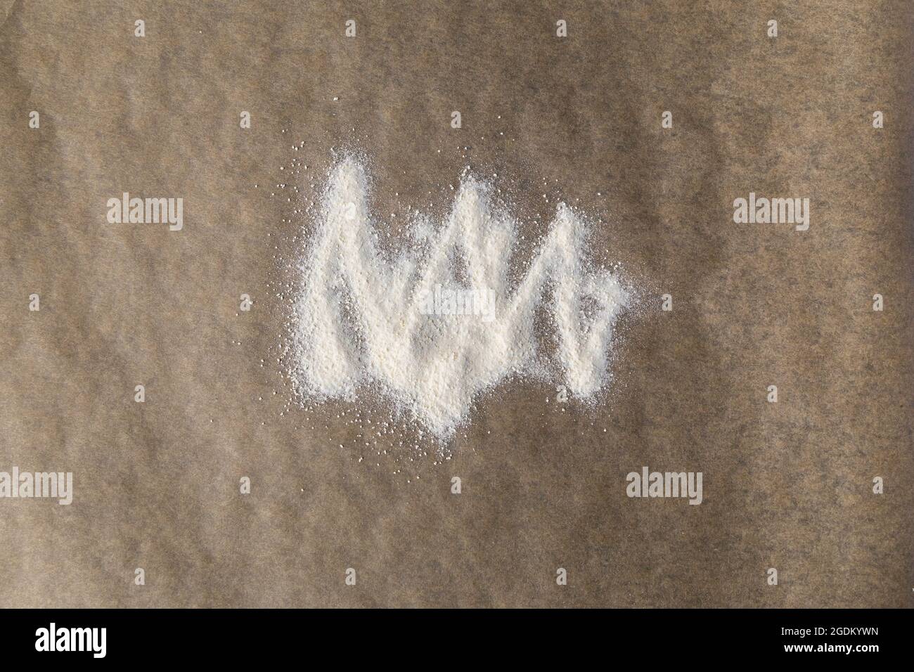 Weißes Mehl auf braunem Backpapier, von oben gesehen. Abstrakter Hintergrund, Draufsicht. Stockfoto