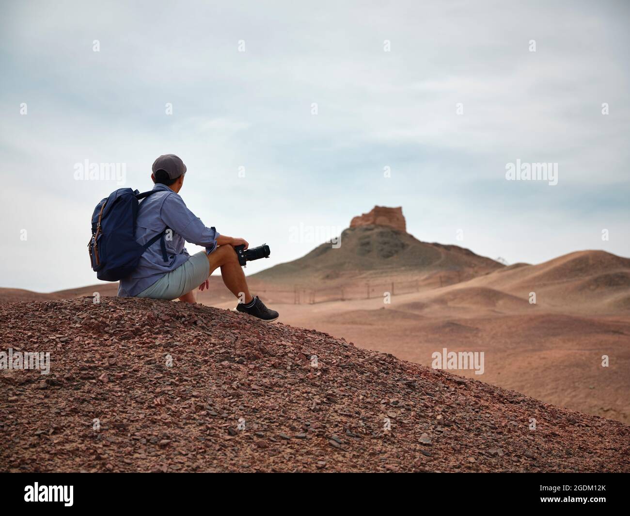 asiatischer männlicher Backpacker Landschaftsfotograf, der auf einem Hügel sitzt und die Aussicht, die Seitenansicht, betrachtet Stockfoto