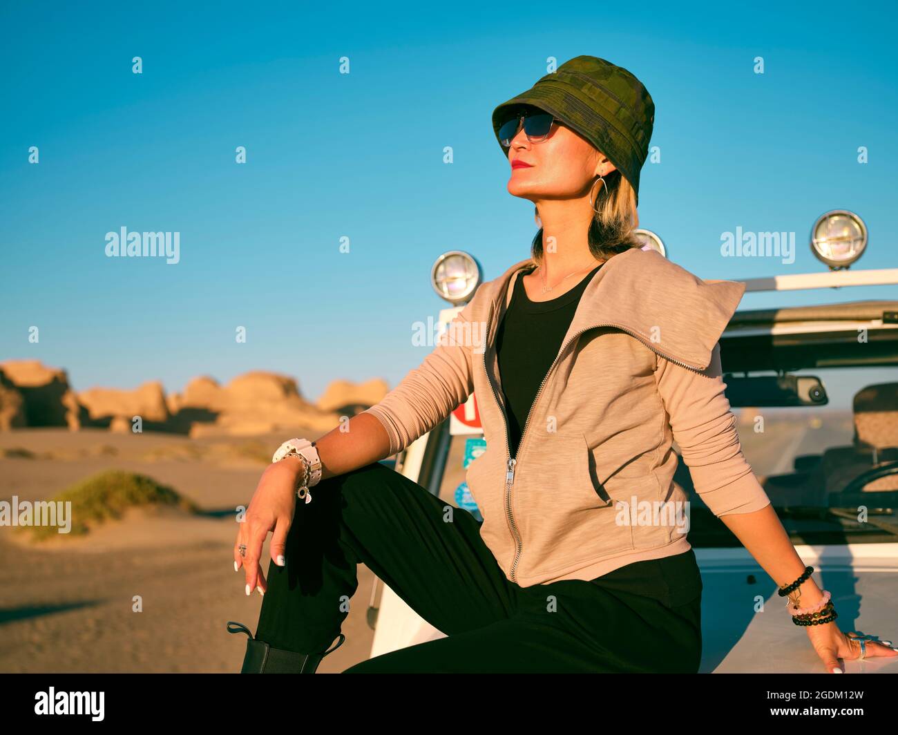 Modische asiatische Frau, die auf der Motorhaube eines Autos im geologischen Nationalpark sitzt Stockfoto