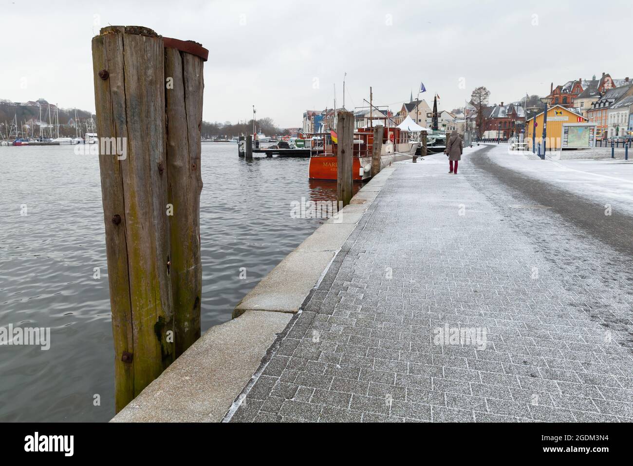 Flensburg, Deutschland - 8. Februar 2017: Küstenansicht von Flensburg mit im Wasser stehenden hölzernen Ankersäulen gehen gewöhnliche Menschen die Straße entlang Stockfoto