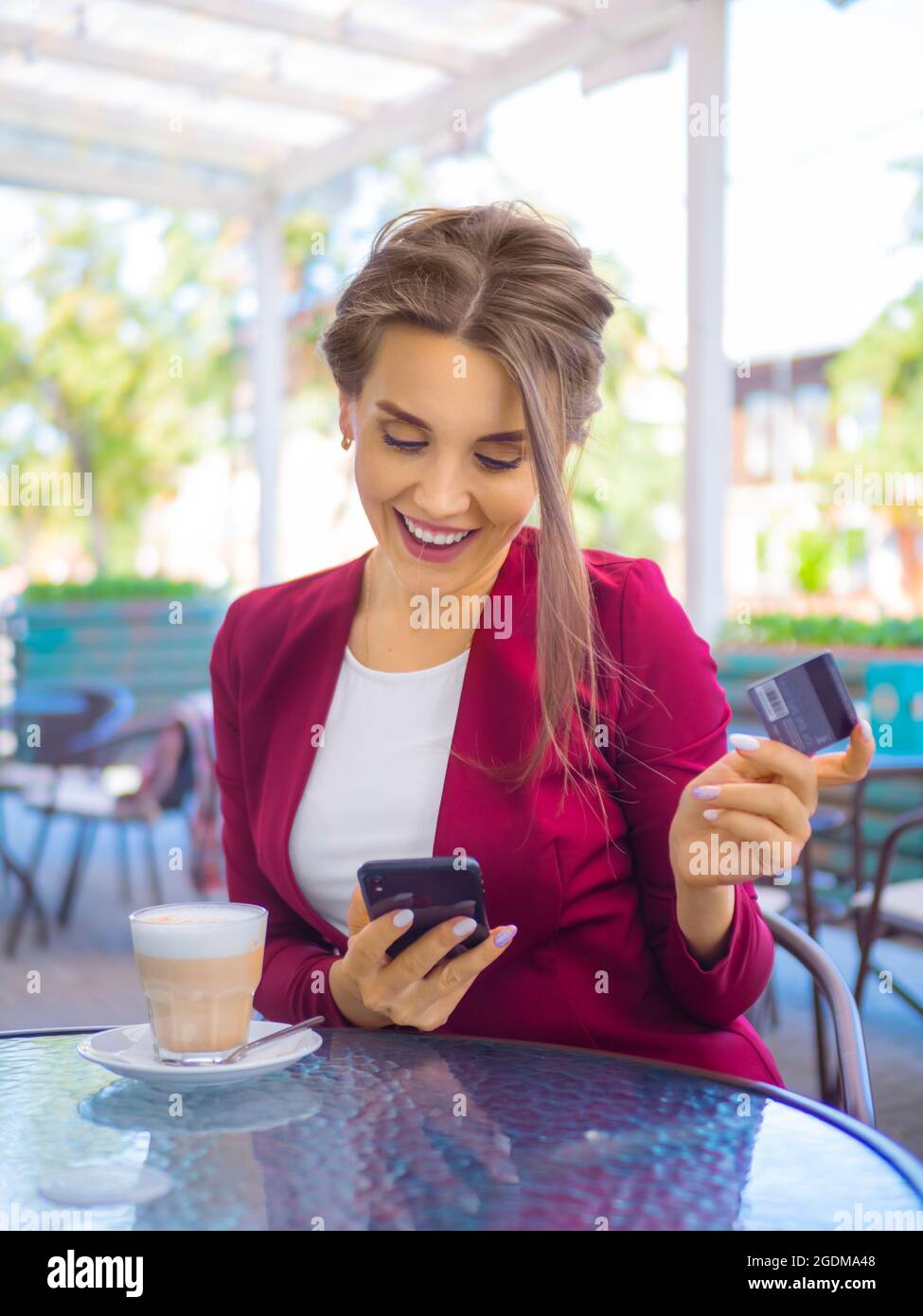 Fröhliche lächelnde Frau mit Smartphone und Kreditkarte während der Kaffeepause. Online-Shopping und Online-Handel Konzept. Stockfoto