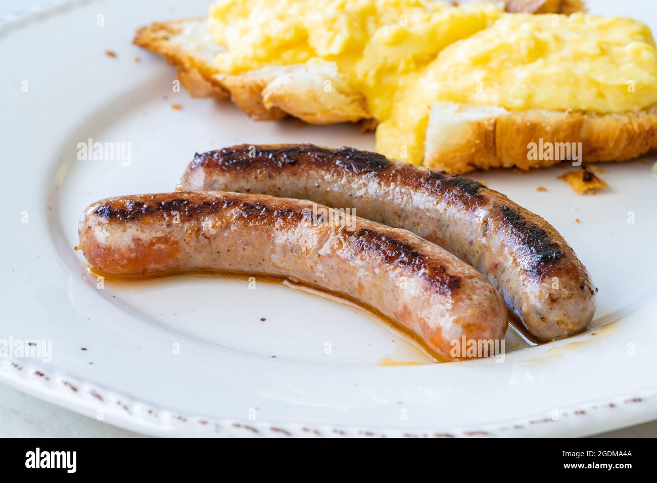 Merguez-Wurst mit Rührei und Croissant auf Frühstücksteller. Bereit zum Essen. Stockfoto