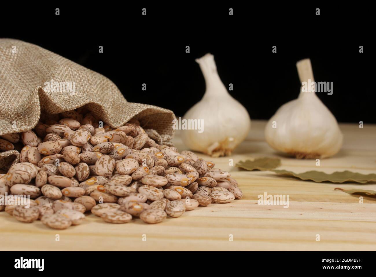 Pinto Bohnen in Burlap Sac mit Knoblauch und Lorbeerblättern im Hintergrund Stockfoto