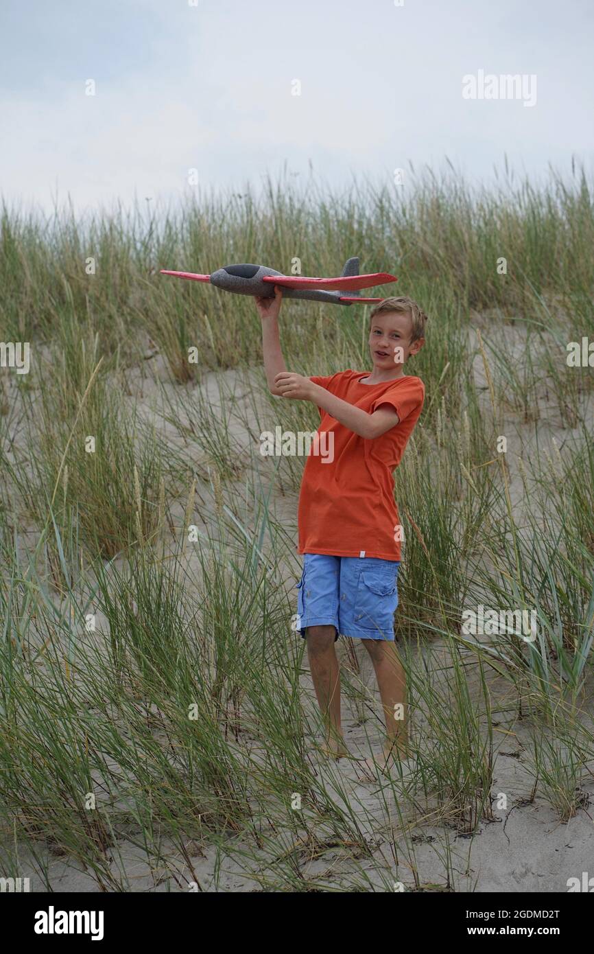 Der 11-jährige Junge spielt mit einem Modell-Segelflugzeug in der Düne gegen den Himmel Stockfoto