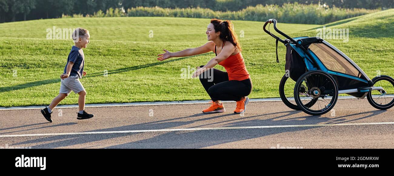 Aktive Mutter mit Kind mit Jogging-Kinderwagen zum Laufen im Park. Glückliche Mutter und ihr Sohn haben Spaß im Freien Stockfoto