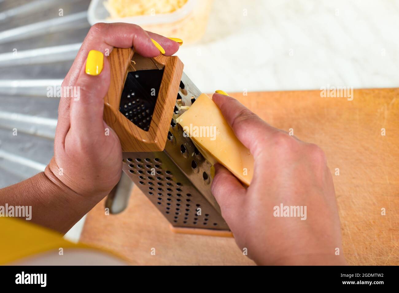 Weibliche Hände reiben einen Käse mit Reibe, Nahaufnahme yup auf einem Holzbrett. Stockfoto