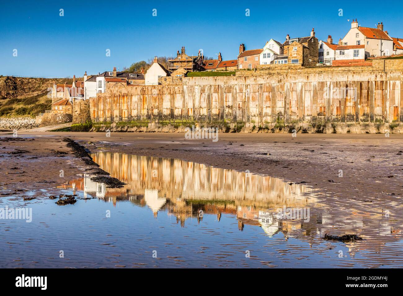 Die Meeresmauer und das Dorf Robin Hood's Bay, North Yorkshire, vom Vorland an einem Frühlingsmorgen, mit Reflexionen in einem Pool. Stockfoto