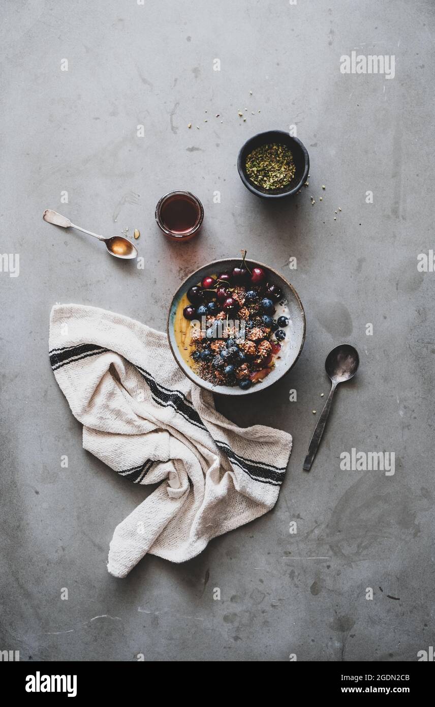 Gesund vegan Frühstück. Flachbild-lay von Quinoa Hafer Müsli coconut Joghurt Schale mit Obst, Honig, Samen, Nüsse, Beeren über grauer Beton Tabelle Hintergrund Stockfoto