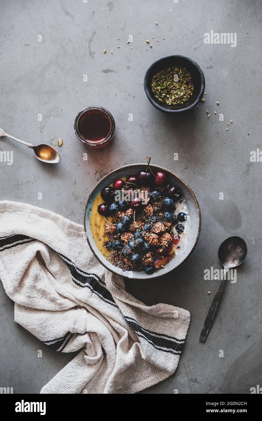 Gesund vegan Frühstück. Flachbild-lay von Quinoa Hafer Müsli coconut Joghurt Schale mit Obst, Honig, Samen, Nüsse, Beeren über grauer Beton Tabelle Hintergrund Stockfoto