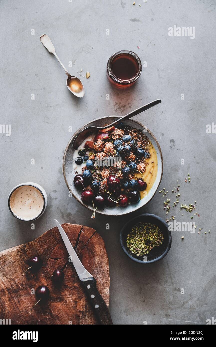 Gesund vegan Frühstück. Flachbild-lay von Quinoa Hafer Müsli coconut Joghurt Schale mit frischen Früchten, Samen, Mutter, Beeren und Tasse Kaffee über Grau backgroun Stockfoto