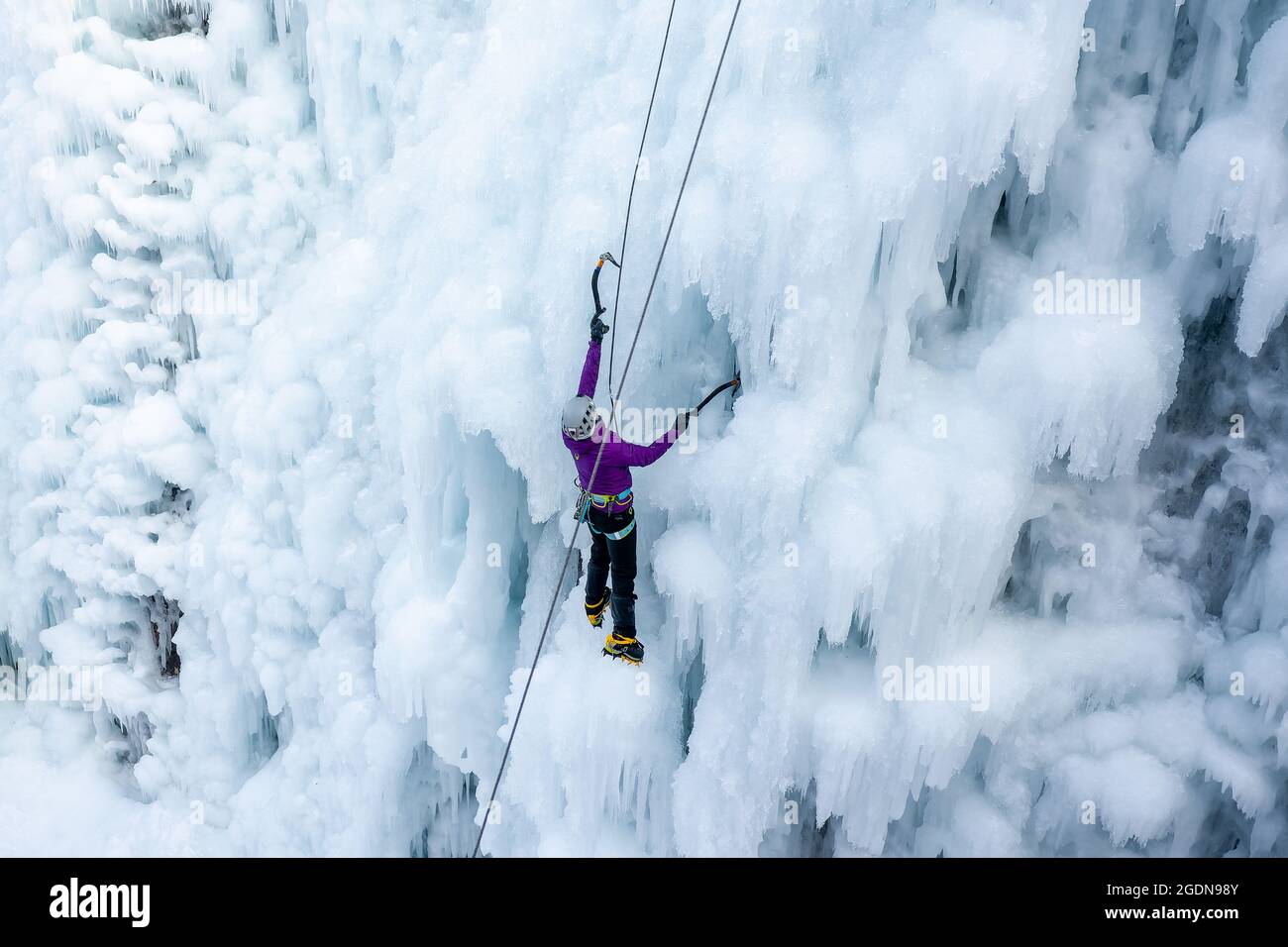 Low-Angle-Aufnahme einer alpinistischen Frau mit Eiskletterausrüstung, Axt und Kletterseilen, Klettern an einem gefrorenen Wasserfall, Blick von unten Stockfoto