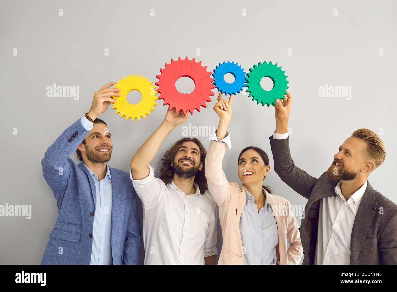 Lächelnde Kollegen verbinden Zahnrad und suchen nach einer Lösung Stockfoto