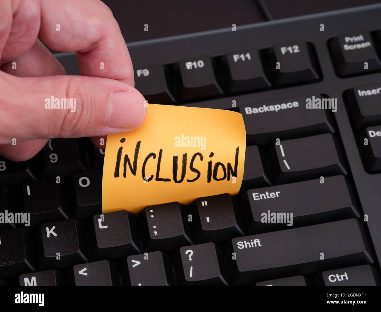 Eine Person, die ein Blatt Papier mit dem Wort „Inklusion“ zwischen den Tasten einer schwarzen Computertastatur hält. Nahaufnahme. Stockfoto
