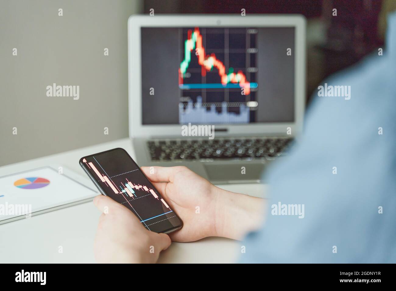 Moderner junger Investor, der Diagramme auf Smartphone und Laptop überprüft Stockfoto