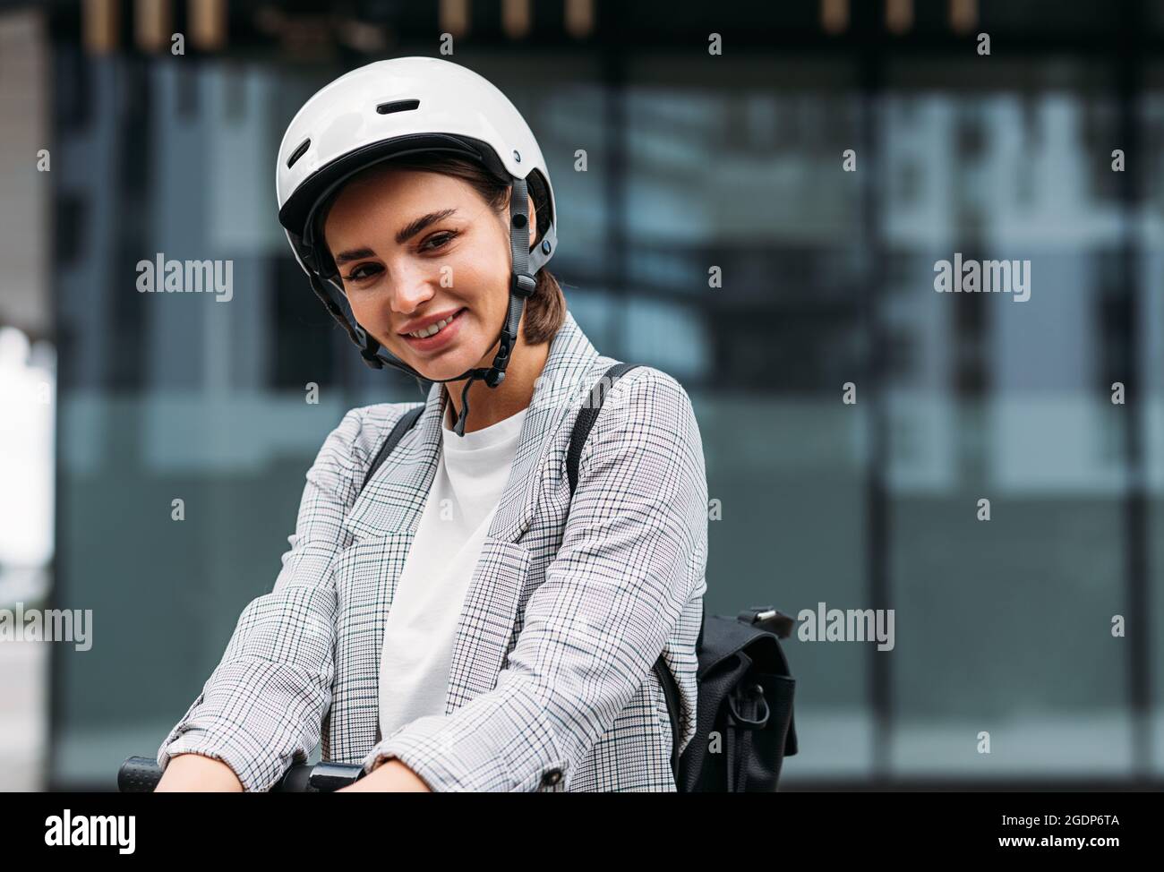 Schöne lächelnde Geschäftsfrau im Fahrradhelm lehnen sich auf Lenker des Elektrorollers Blick auf die Kamera Stockfoto