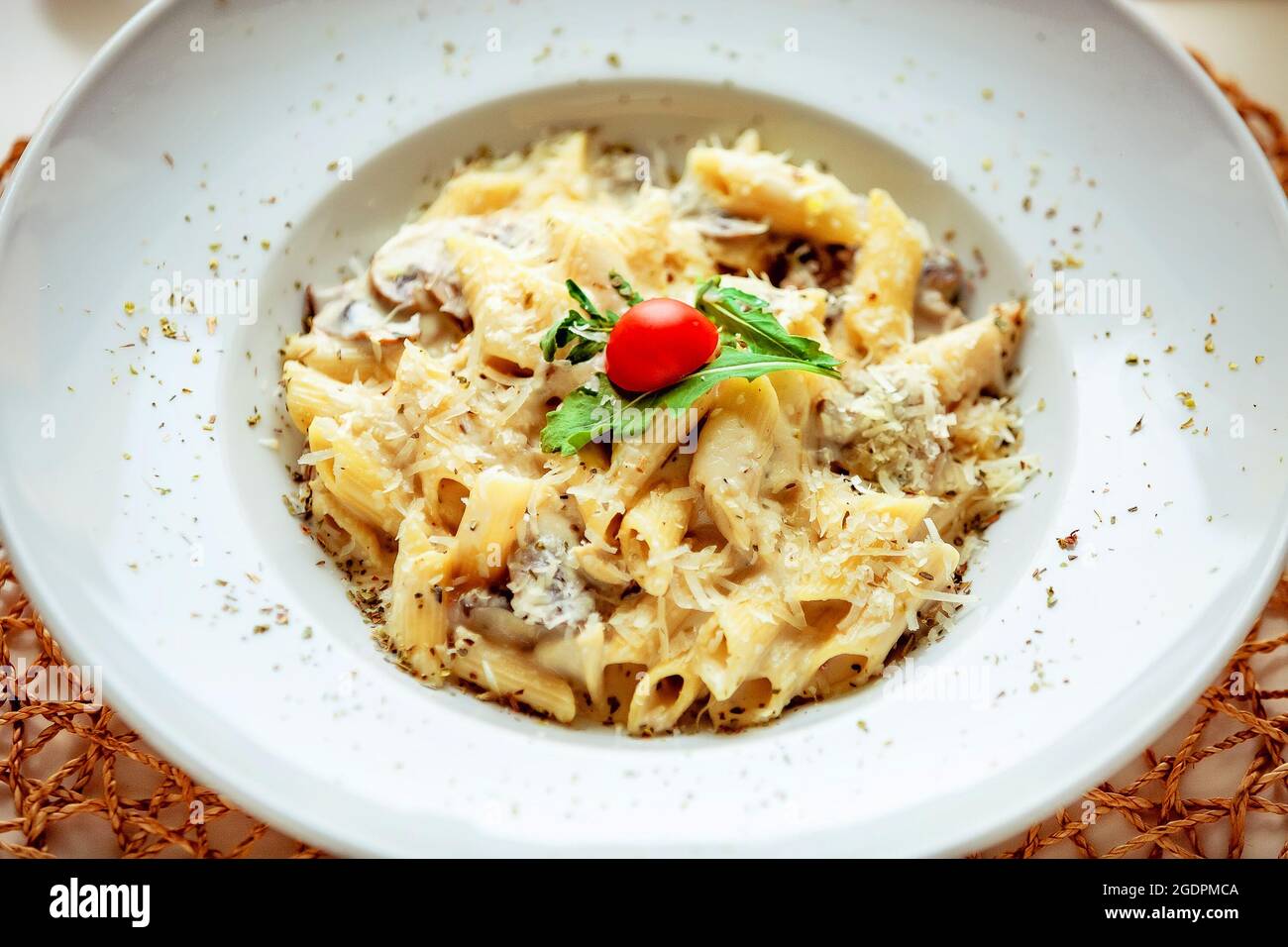 Pasta mit Pilzen in einer weißen Sauce, garniert mit einer Scheibe Kirschtomate und einem Blatt Kräuter Stockfoto