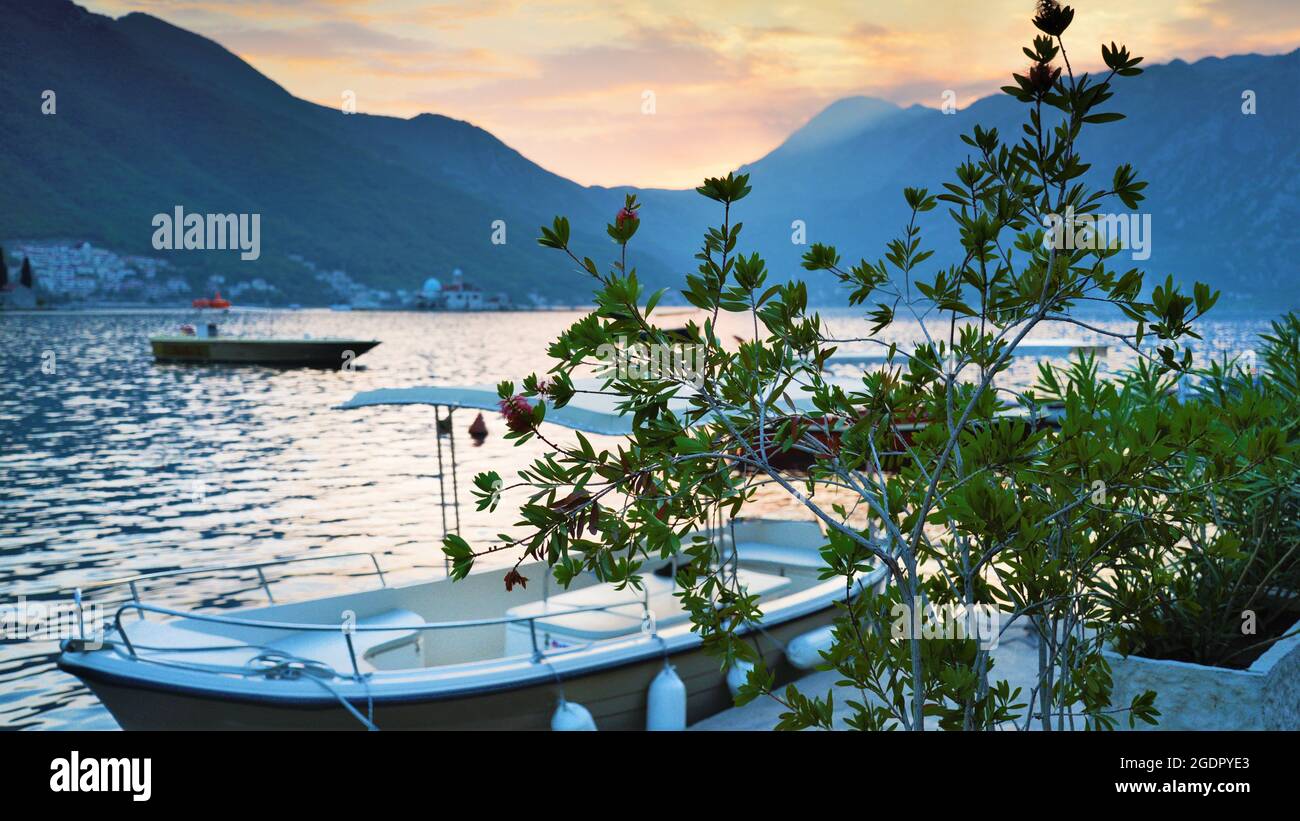 Wunderschöne Abenddämmerung beschauliches Wasser und untergehende Sonne hinter fernen Bergen, Boote und Laub im Vordergrund. Stockfoto