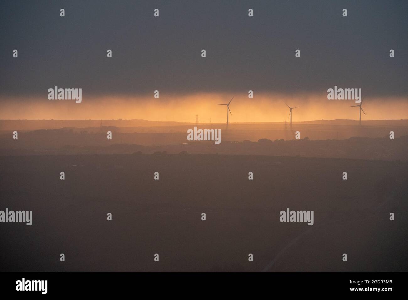 Eine Reihe von Windturbinen, die die späte Abendsonne unter dunklen und launischen Wolken fangen Stockfoto