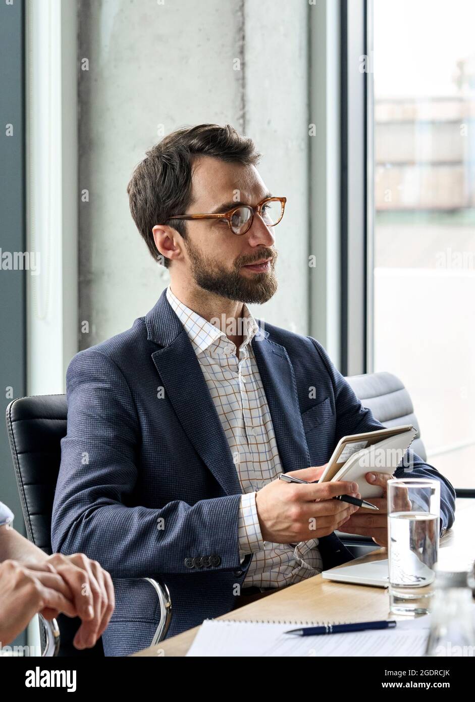 Ernsthafter männlicher ceo, der einen Kollegen mit einem Notizbuch bei der Tischsitzung ansieht. Stockfoto