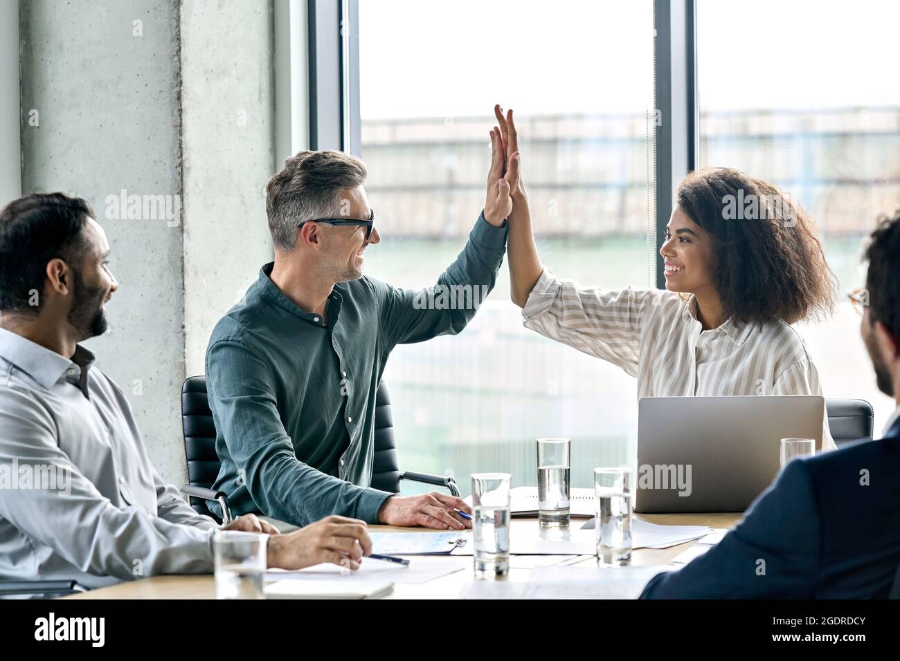 Glückliche internationale Geschäftsleute, die am Tisch des Tagungsraums fünf hohe Sterne geben. Stockfoto