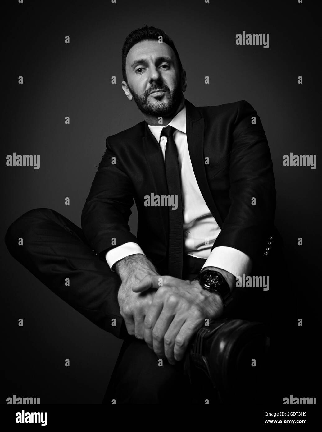 Schwarz und Weiß. Selbstbewusster, kraftvoller Geschäftsmann in modernem Büroanzug sitzt mit gekreuzten Beinen und hält den Fuß Stockfoto