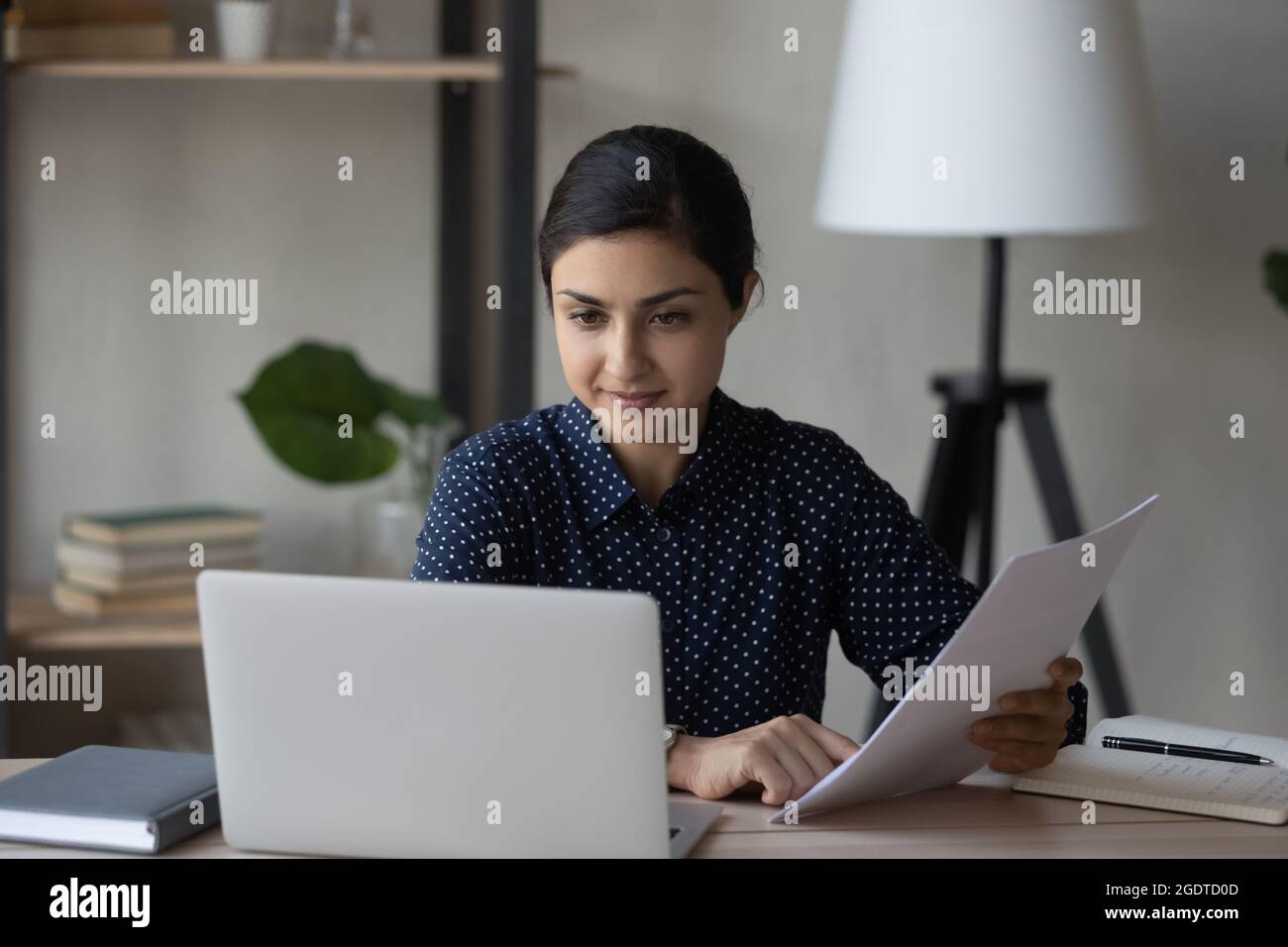 Junge indische Geschäftsfrau arbeitet mit Papierkram am Laptop Stockfoto