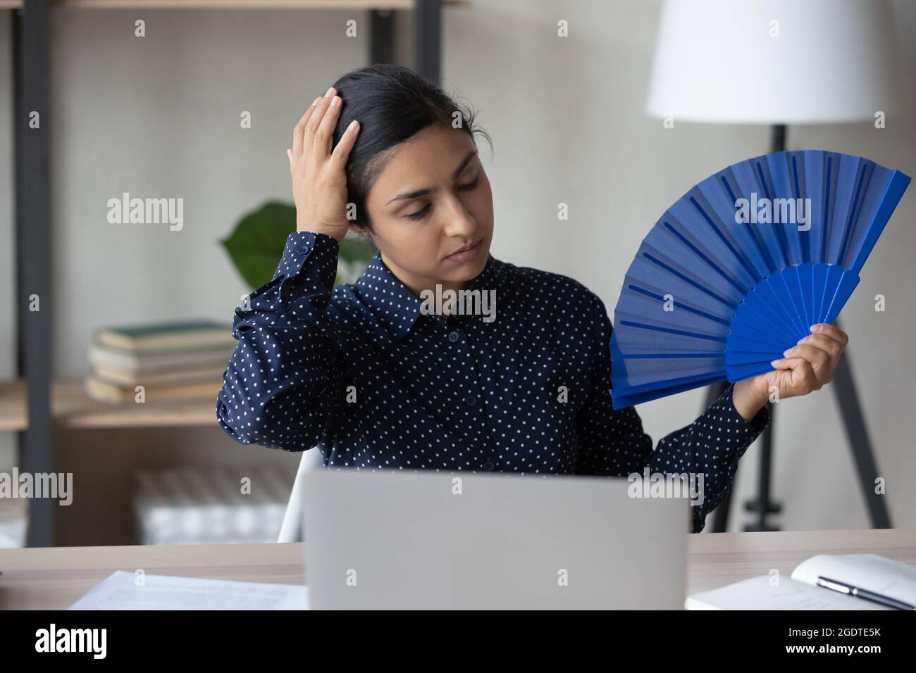 Unwell indische Frau winken mit Handventilator am Arbeitsplatz Stockfoto