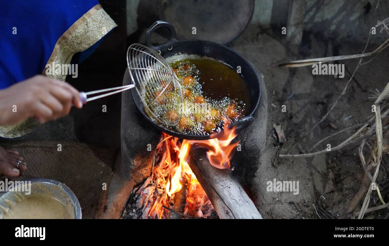 Frau braten Lebensmittel mit Senföl auf dem Ofen. Typischer Holzofen oder Chulha, der im ländlichen indien zum Kochen verwendet wird. Stockfoto